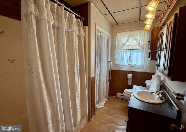 bathroom with toilet, vanity, a drop ceiling, a baseboard heating unit, and hardwood / wood-style flooring