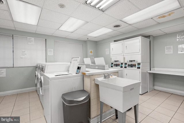 laundry area with stacked washing maching and dryer, washing machine and dryer, light tile patterned flooring, and sink