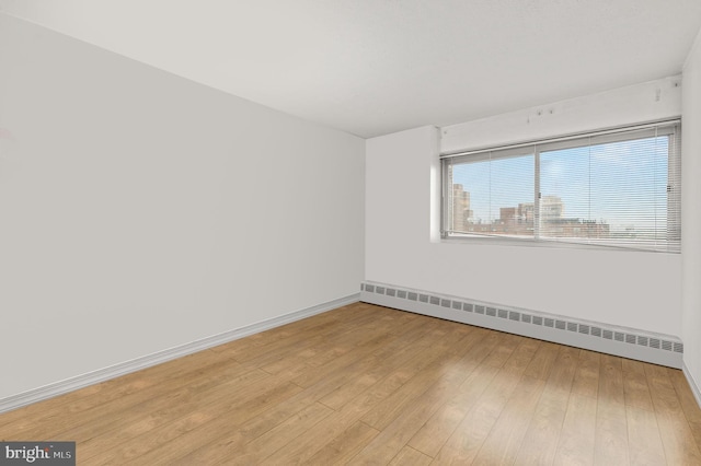 unfurnished room featuring baseboard heating and wood-type flooring