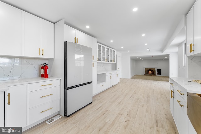 kitchen with tasteful backsplash, light hardwood / wood-style flooring, white cabinets, light stone counters, and white refrigerator