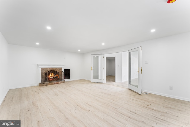 unfurnished living room featuring french doors, a premium fireplace, and light hardwood / wood-style floors