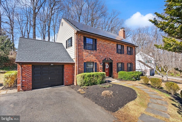 view of front facade with a garage, solar panels, brick siding, driveway, and a chimney