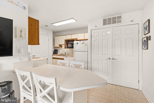 kitchen with sink, white appliances, kitchen peninsula, and a breakfast bar