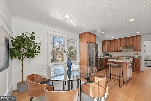 kitchen featuring a kitchen island, decorative backsplash, stainless steel appliances, crown molding, and light hardwood / wood-style flooring