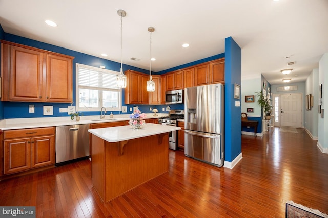 kitchen with appliances with stainless steel finishes, dark hardwood / wood-style flooring, a kitchen island, pendant lighting, and sink