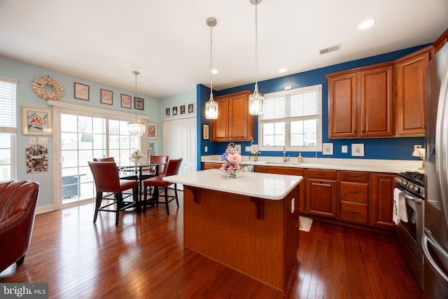 kitchen featuring stainless steel range with gas stovetop, dark hardwood / wood-style flooring, hanging light fixtures, a kitchen island, and sink