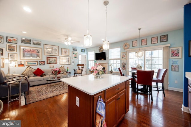 kitchen with dark hardwood / wood-style floors, pendant lighting, ceiling fan with notable chandelier, and a kitchen island