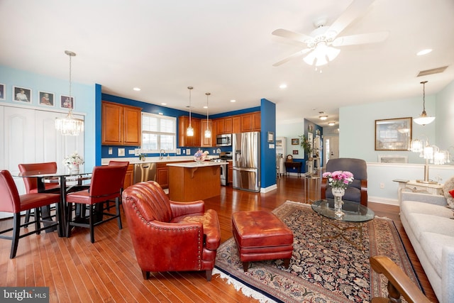 living room featuring ceiling fan with notable chandelier, hardwood / wood-style flooring, and sink