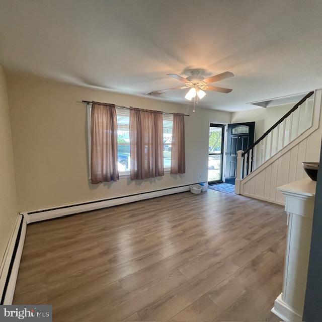 unfurnished living room featuring ceiling fan, baseboard heating, and hardwood / wood-style flooring