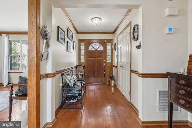 entryway featuring baseboards, wood-type flooring, visible vents, and crown molding