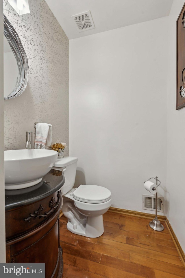 half bath featuring visible vents, vanity, toilet, and hardwood / wood-style flooring