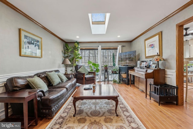 living room featuring a skylight, ornamental molding, wood finished floors, and wainscoting