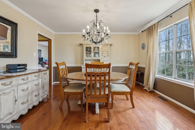 dining space featuring a notable chandelier, visible vents, baseboards, ornamental molding, and light wood-type flooring