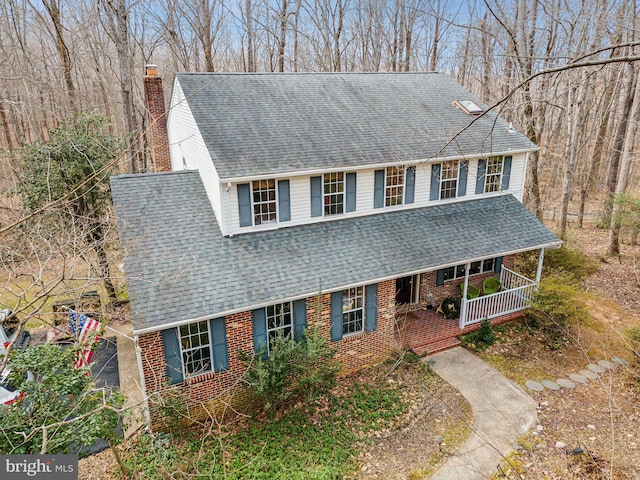 view of front facade featuring a chimney, brick siding, roof with shingles, and a porch