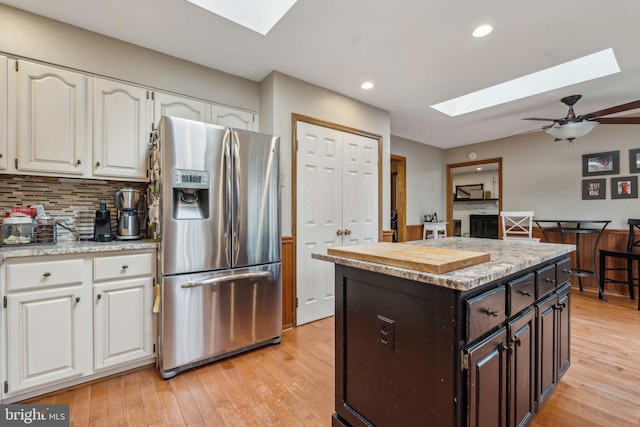 kitchen featuring a skylight, white cabinets, light wood-type flooring, tasteful backsplash, and stainless steel fridge