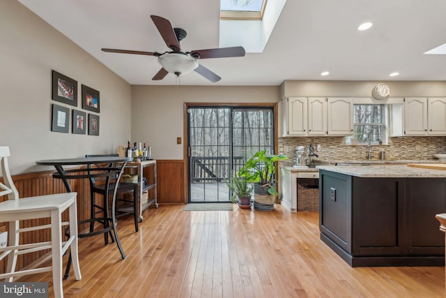 kitchen featuring wainscoting, light wood-type flooring, a skylight, and white cabinetry