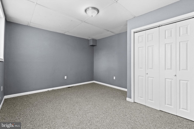 unfurnished bedroom featuring a drop ceiling, dark carpet, and a closet