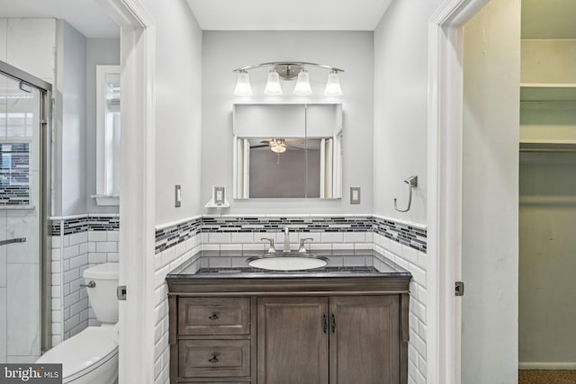 bathroom featuring toilet, tile walls, vanity, a shower with door, and ceiling fan