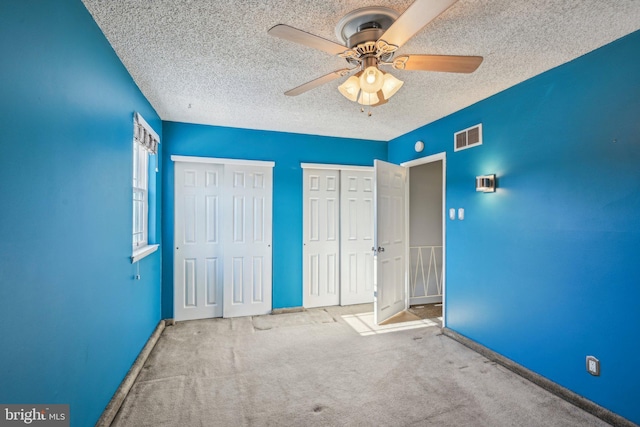 unfurnished bedroom with two closets, light colored carpet, a textured ceiling, and ceiling fan