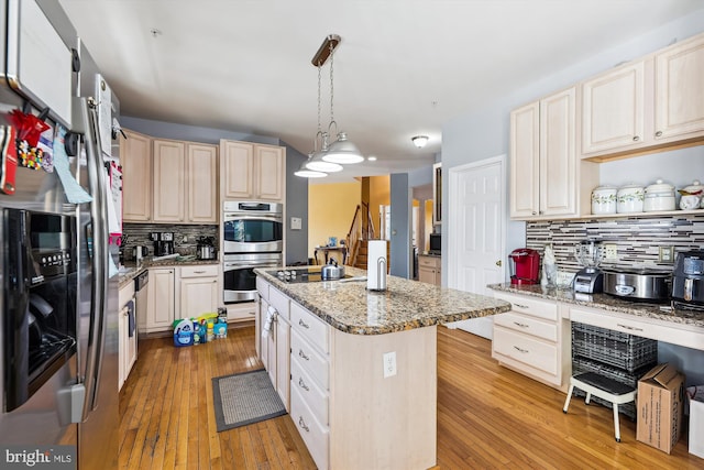 kitchen featuring decorative light fixtures, backsplash, light stone countertops, an island with sink, and stainless steel appliances