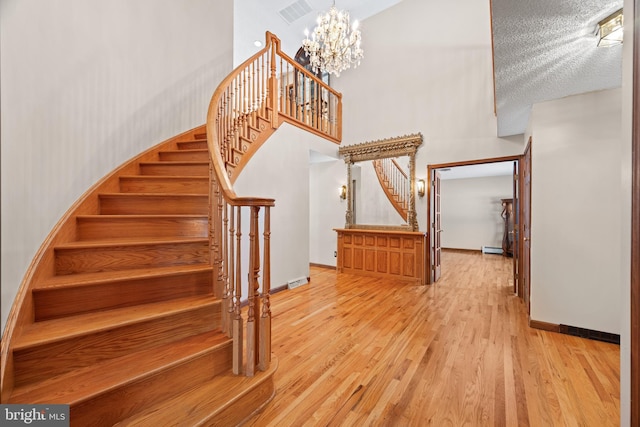 stairway with baseboard heating, a chandelier, and hardwood / wood-style flooring