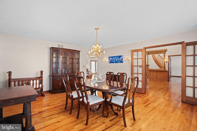 dining area with french doors, an inviting chandelier, a textured ceiling, and light hardwood / wood-style floors