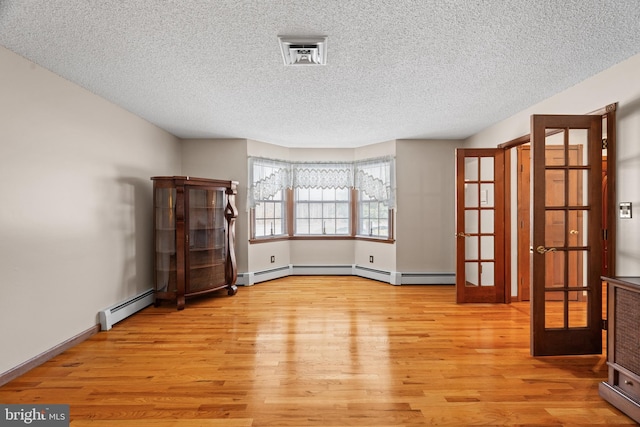 spare room with light wood-type flooring, a baseboard heating unit, french doors, and a textured ceiling