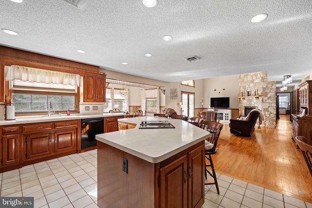 kitchen with dishwasher, a center island, a fireplace, a breakfast bar, and light tile patterned floors