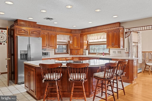 kitchen featuring light tile patterned floors, stainless steel fridge, a breakfast bar area, sink, and a center island