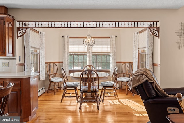 dining area featuring a textured ceiling, baseboard heating, light hardwood / wood-style flooring, and an inviting chandelier