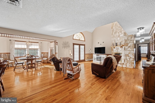 living room with vaulted ceiling, a fireplace, light hardwood / wood-style flooring, a textured ceiling, and french doors