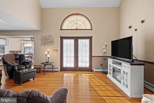 living room featuring baseboard heating, wood-type flooring, a towering ceiling, and french doors