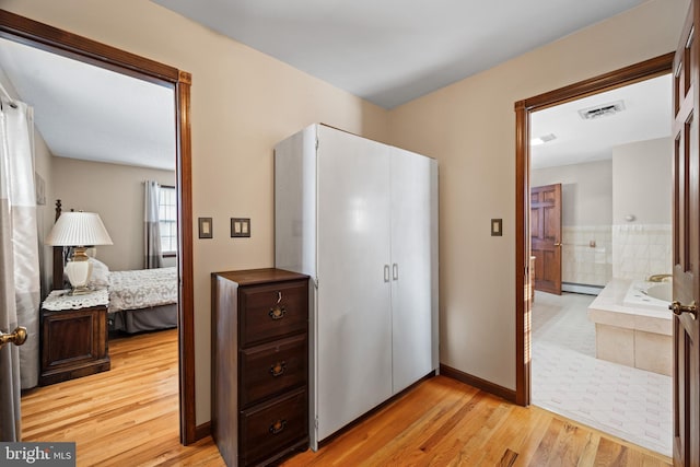 bedroom featuring light wood-type flooring, ensuite bath, and baseboard heating