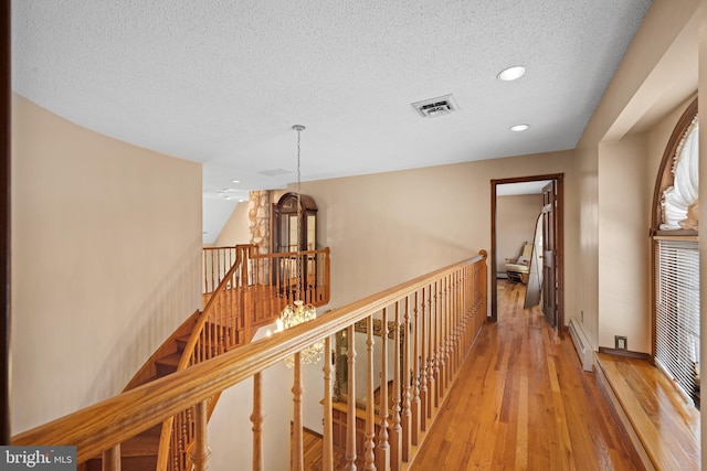 corridor featuring light hardwood / wood-style floors, a baseboard radiator, a textured ceiling, and a notable chandelier