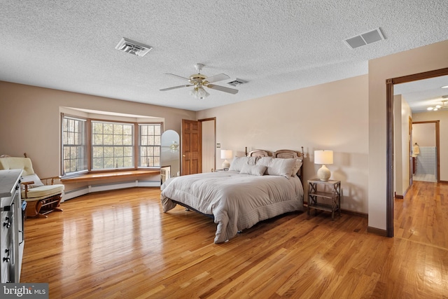 bedroom featuring ceiling fan, light wood-type flooring, baseboard heating, and a textured ceiling