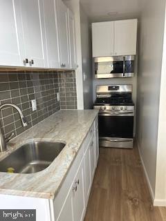 kitchen with appliances with stainless steel finishes, backsplash, light stone countertops, white cabinets, and sink