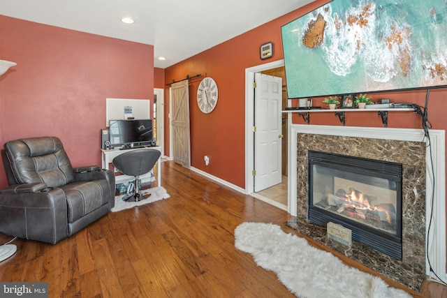 living room with a high end fireplace, a barn door, and wood-type flooring