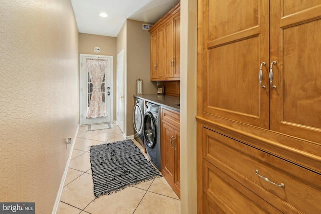 clothes washing area with light tile patterned floors, washer and dryer, and cabinets