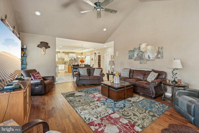 living room with ceiling fan with notable chandelier, hardwood / wood-style flooring, and high vaulted ceiling