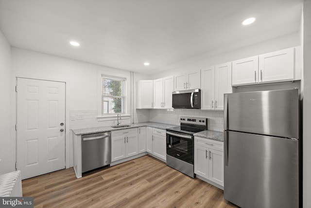 kitchen featuring white cabinets, sink, backsplash, stainless steel appliances, and light stone counters