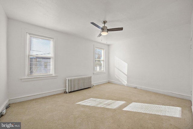 unfurnished room featuring a healthy amount of sunlight, light colored carpet, radiator, and ceiling fan