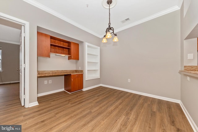 kitchen with crown molding, decorative light fixtures, built in features, hardwood / wood-style flooring, and built in desk