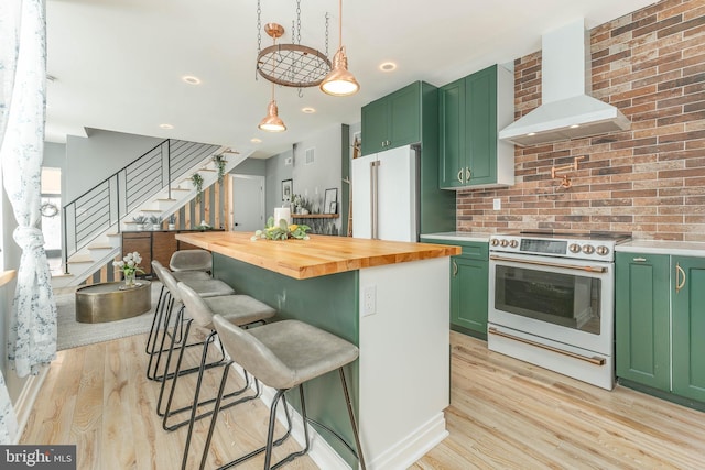 kitchen featuring white appliances, butcher block counters, wall chimney range hood, and green cabinets