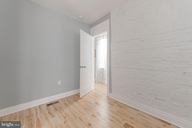 spare room with brick wall and light hardwood / wood-style floors