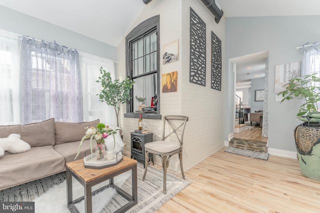 living room featuring brick wall, light hardwood / wood-style flooring, vaulted ceiling, and a wood stove