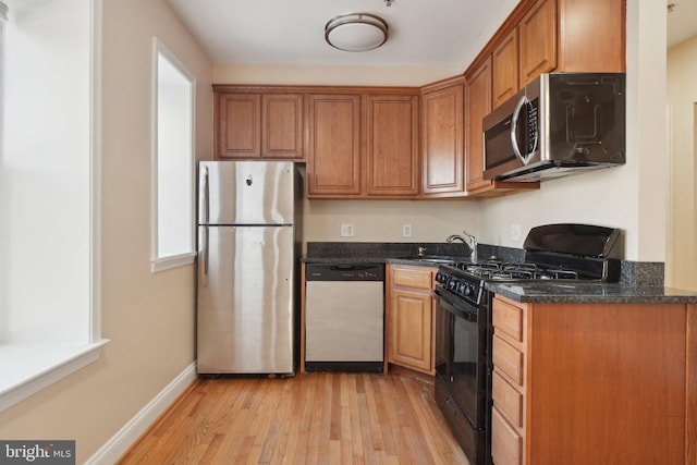 kitchen with dark stone counters, sink, stainless steel appliances, and light hardwood / wood-style flooring