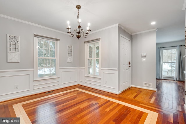 entryway featuring hardwood / wood-style flooring, crown molding, plenty of natural light, and an inviting chandelier