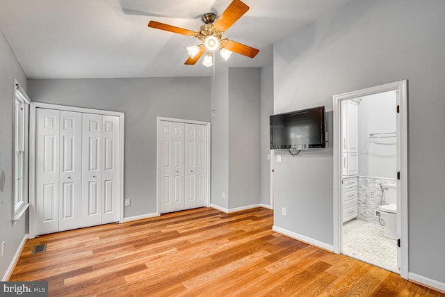 unfurnished bedroom featuring ceiling fan, two closets, light hardwood / wood-style flooring, and ensuite bath