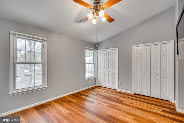 unfurnished bedroom with ceiling fan, two closets, light hardwood / wood-style flooring, and vaulted ceiling