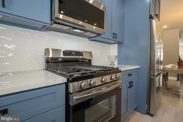 kitchen featuring light wood-type flooring, appliances with stainless steel finishes, blue cabinetry, and light stone counters